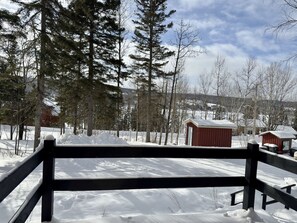 A snow-covered landscape with a wooden fence, a red building, and tall trees. - Mini Chalet at Lake Pohénégamook, a Peaceful Haven! #1 (Pohénégamook)