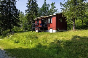 A cabin with a balcony, surrounded by trees and grass. - Mini Chalet at Lake Pohénégamook, a Peaceful Haven! #1 (Pohénégamook)