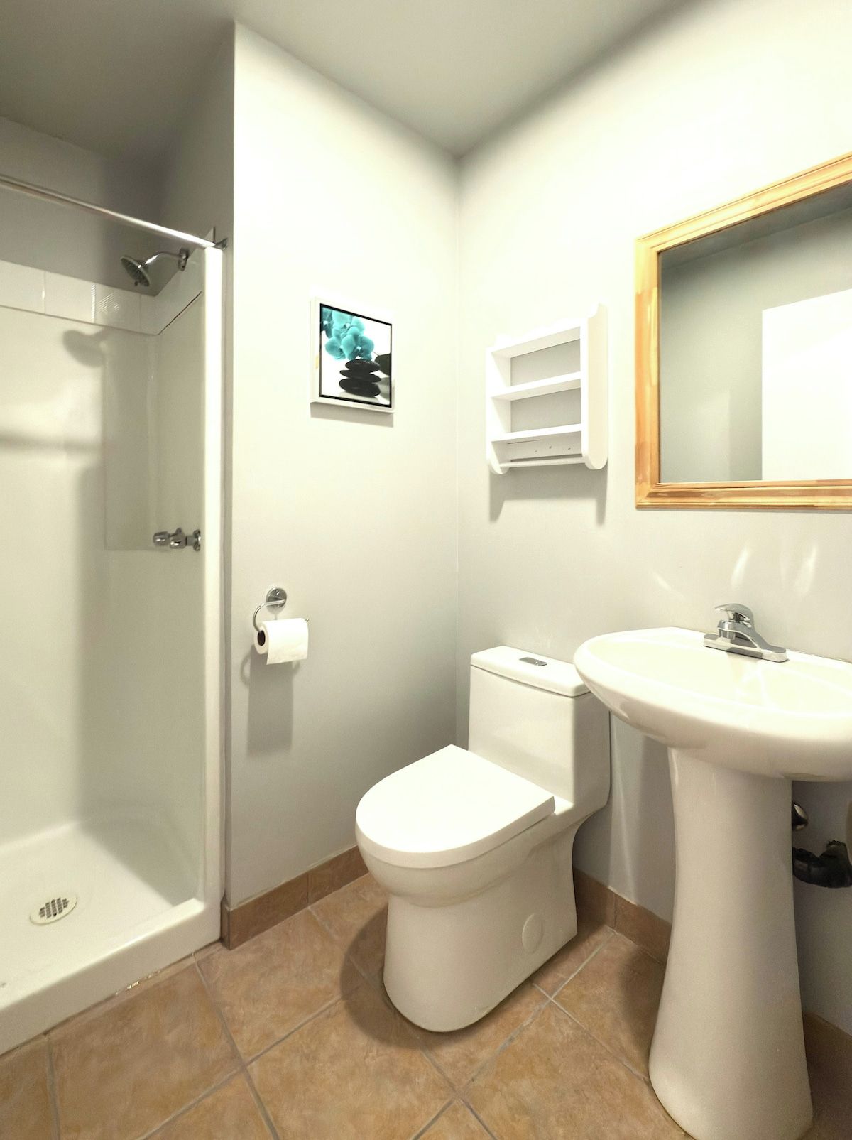 A bathroom with a shower, toilet, sink, and a framed picture on the wall.