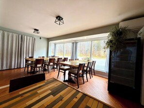 Un espace repas avec une grande table et des chaises, un plancher en bois et une vue par la fenêtre.