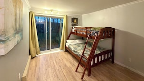 Una habitació amb literes, una finestra corredissa que dona a un balcó i un quadre a la paret.