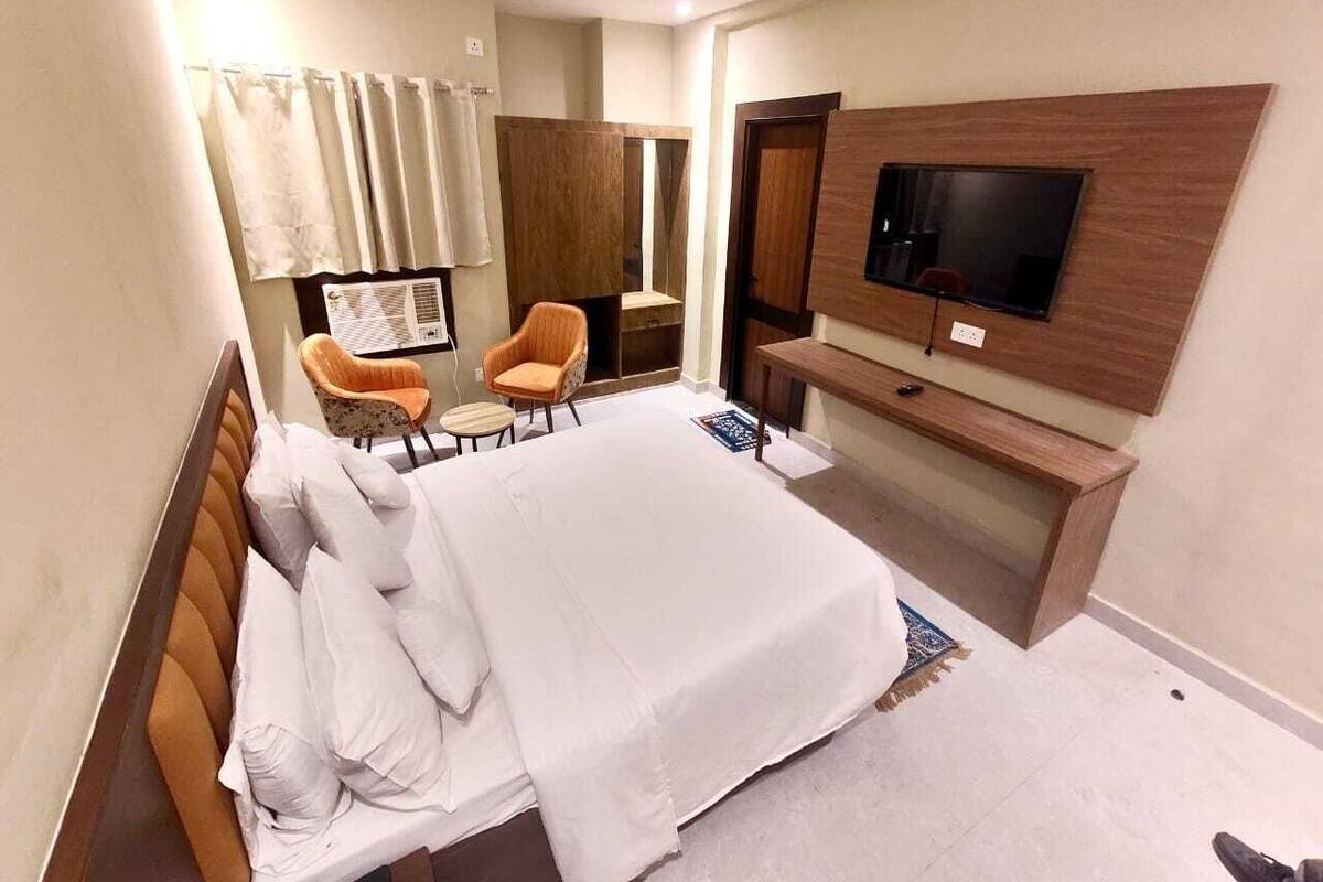 A hotel room with a bed, a TV mounted on the wall, a desk, and two chairs.