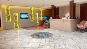 Uma área de recepção de hotel com chão de mármore, balcão de recepção e uma televisão na parede.