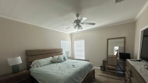 Un dormitorio con cama, mesitas de noche, escritorio, silla, espejo y ventilador de techo.