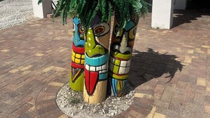 Un edificio con un porche cubierto, una palmera y totems decorativos.