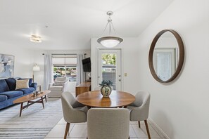A living room with a sofa, coffee table, and chairs. There is a dining table with a vase. A large mirror hangs on the wall. - 2-BD 2-BA condo in the fantastic Catalina Foothills, 2 pools & fitness Ctr gated (Tucson)