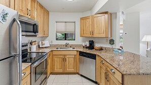Cozinha moderna com armários de madeira, eletrodomésticos de aço inoxidável, bancadas de granito e uma janela com vista.