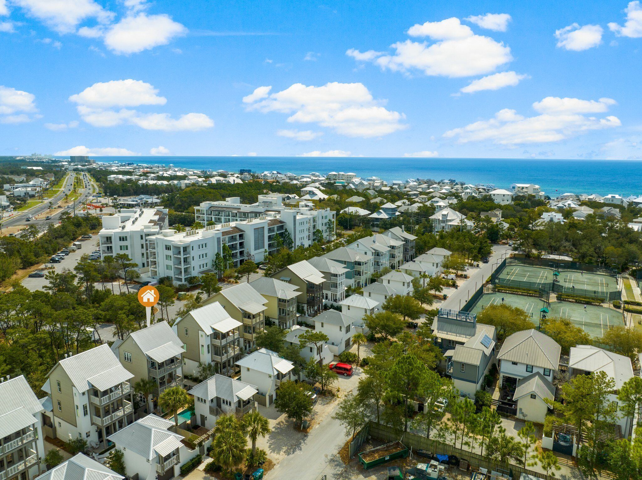 A coastal residential area with multiple-story buildings, a tennis court, and a clear view of the ocean.