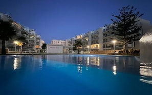 Une piscine avec vue sur des immeubles à plusieurs étages, un panneau indiquant « Marina Real II » et un palmier.