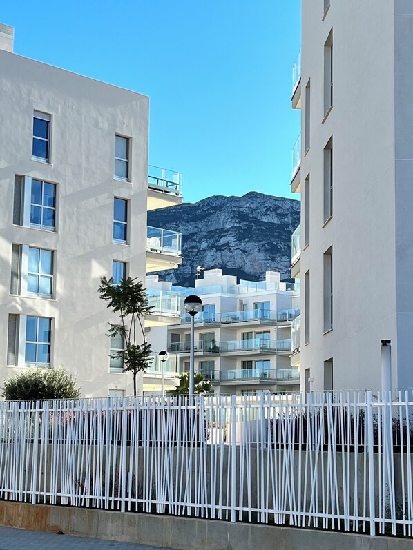 Un bâtiment moderne doté de nombreux balcons, d’une clôture blanche et ayant une montagne en toile de fond.