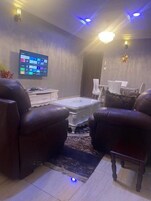 Una sala de estar moderna con un televisor de pantalla plana, sillones de cuero, una mesa de centro y un tapete estampado.