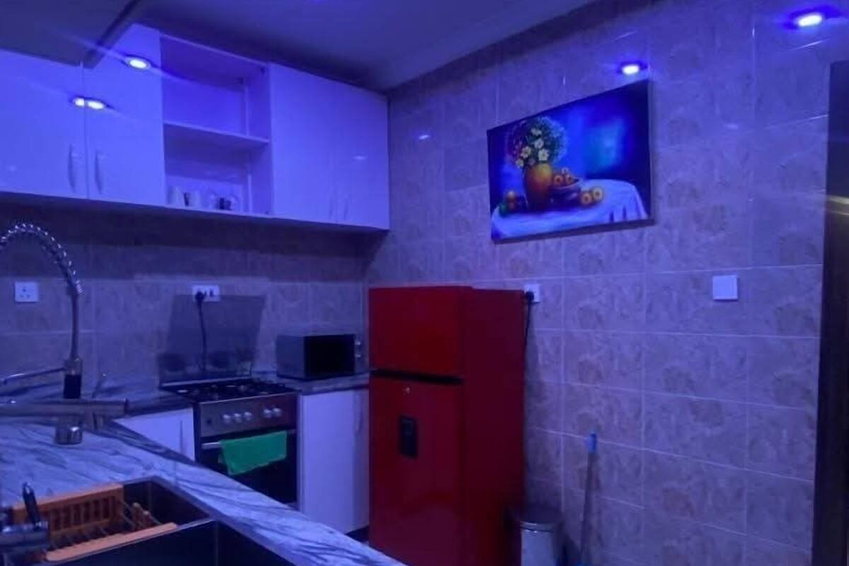 A kitchen with a red refrigerator, a microwave, and a stove. There is a painting on the wall and a broom leaning against the wall.