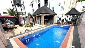 Ein Schwimmbecken mit einer gefliesten Kante, einer kleinen überdachten Sitzgelegenheit und einer Springbrunnen.