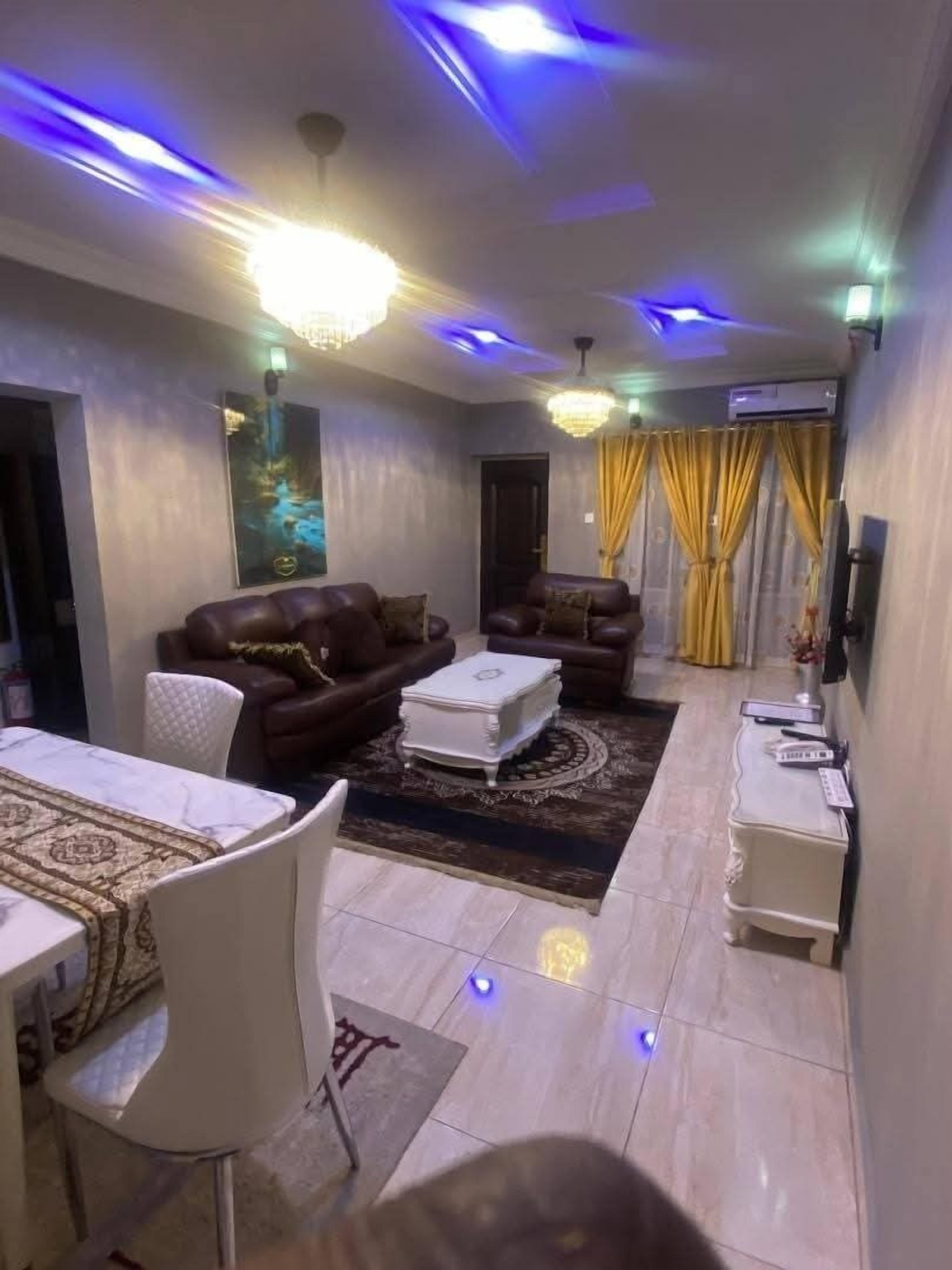 A living room with a brown leather sofa, a white coffee table, and a dining area with a table and chairs.