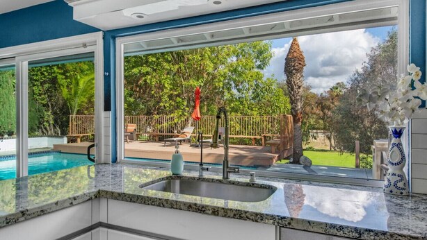 A kitchen with a large window overlooking a pool and a deck area. - MB Sabina - Pool, Fire Pit, Fun For Kids (Mission Viejo)