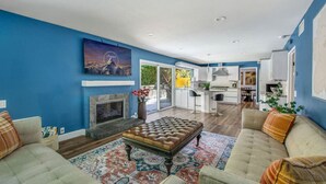 A spacious living room with a fireplace, a large rug, and a dining area with a kitchen in the background. - MB Sabina - Pool, Fire Pit, Fun For Kids (Mission Viejo)