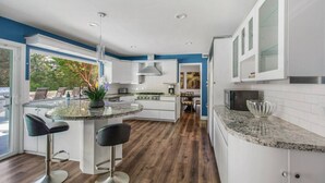 A modern kitchen with white cabinets, granite countertops, and a central island with bar stools. - MB Sabina - Pool, Fire Pit, Fun For Kids (Mission Viejo)