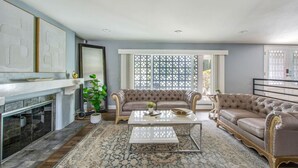 A spacious living room with a fireplace, two sofas, a coffee table, and a large window with a lattice design. - MB Sabina - Pool, Fire Pit, Fun For Kids (Mission Viejo)