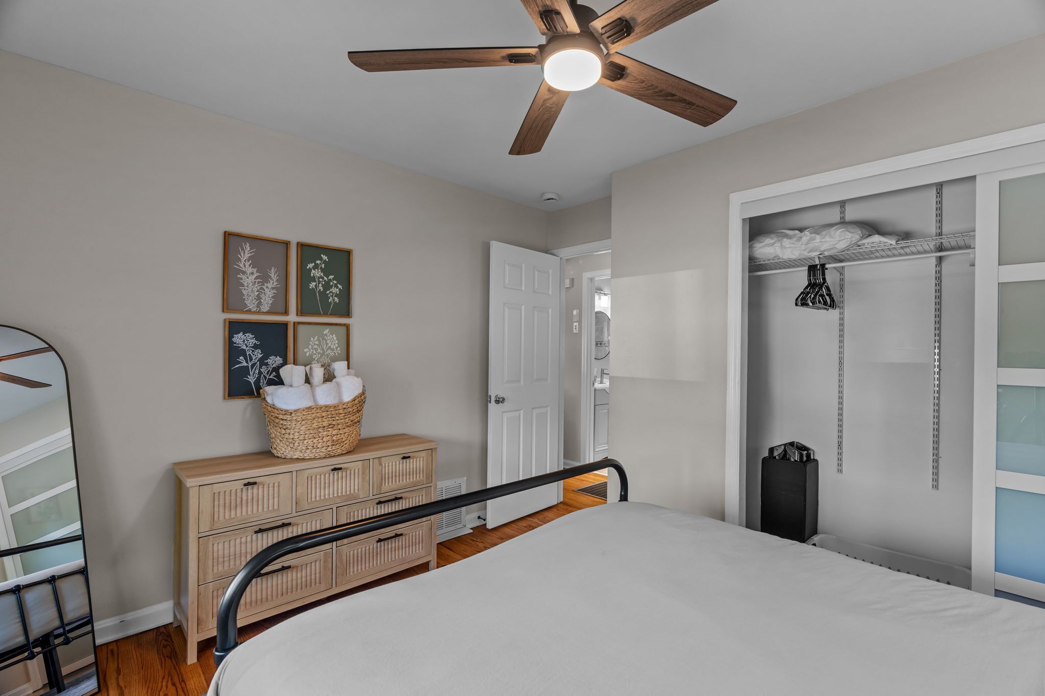 A bedroom with a bed, a wooden dresser, a ceiling fan, and a wall-mounted shelf with towels.
