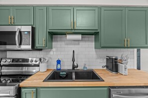 Cocina con gabinetes verdes, electrodomésticos de acero inoxidable y encimera de madera.