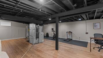 A spacious room with a wooden floor, a standing desk, a chair, a treadmill, and a wall-mounted sign.