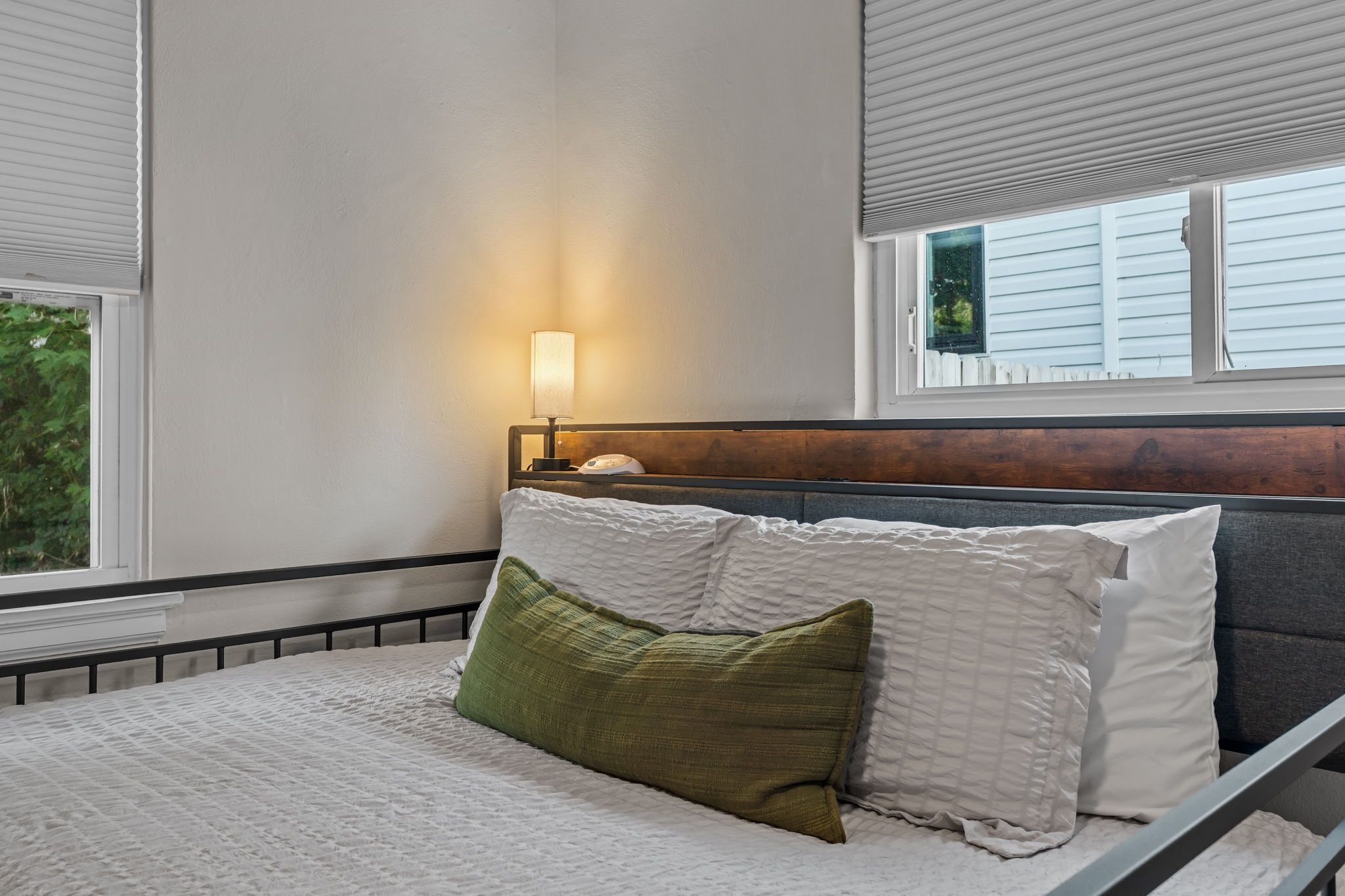 A bedroom with a bed, a nightstand, a lamp, and a window with blinds.