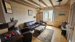 Ein gemütliches Wohnzimmer mit einer Ledersofa, einem Couchtisch und einem Kamin. An den Wänden befinden sich Bilderrahmen und ein großes Fenster lässt natürliches Licht herein.
