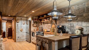 A rustic kitchen with wooden beams, stone walls, and hanging light fixtures. - Boulder Hot Tub Buffalo River Fairy Tale  Cottage (Jasper)