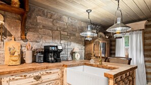 A rustic kitchen with a large wooden island, stone wall, and hanging pendant lights. - Boulder Hot Tub Buffalo River Fairy Tale  Cottage (Jasper)