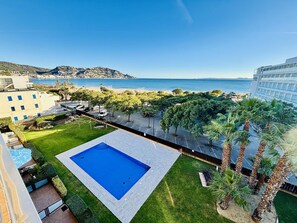A swimming pool surrounded by a well-maintained lawn, with a view of the sea and a distant mountain. - MIL.LENI I. Dúplex con encanto y vistas al mar en Roses – ¡Disfruta del paseo marítimo! (Roses)