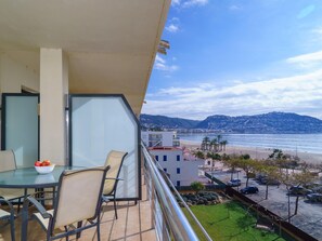 A balcony with a table and chairs, overlooking a beach and a cityscape. - MIL.LENI I. Dúplex con encanto y vistas al mar en Roses – ¡Disfruta del paseo marítimo! (Roses)