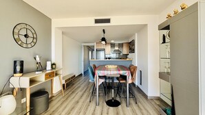 A compact kitchen with a dining area, a clock on the wall, and a small cabinet with decorative items. - MIL.LENI I. Dúplex con encanto y vistas al mar en Roses – ¡Disfruta del paseo marítimo! (Roses)