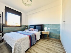 A bedroom with a bed, bedside table, lamp, and a view of the outside through a window. - MIL.LENI I. Dúplex con encanto y vistas al mar en Roses – ¡Disfruta del paseo marítimo! (Roses)