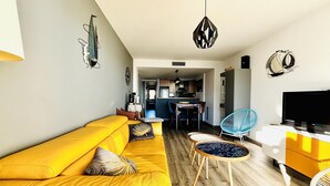 A living room with a yellow sofa, a dining table, chairs, a TV, and a kitchen in the background. - MIL.LENI I. Dúplex con encanto y vistas al mar en Roses – ¡Disfruta del paseo marítimo! (Roses)