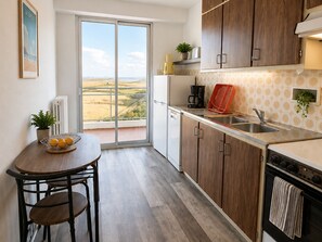 A compact kitchen with a view of the countryside, a dining area with a table and chairs, and wooden cabinets. - Bright 4-person apartment, sea view with parking (Saint-Brevin-les-Pins)
