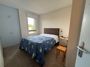 Een slaapkamer met een bed, nachtkastje, houten stoel, garderobe en een raam.
