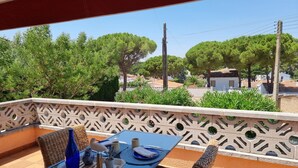 Un balcone con un tavolo apparecchiato per due, una sedia in vimini e vista su alberi e palazzi.