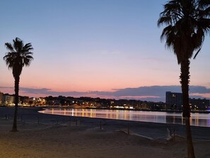 A beach with palm trees, a calm sea, and city lights in the background. - Family house with terrace and pool in L'Escala (L'Escala)