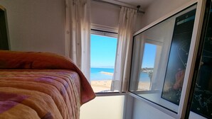 Une chambre avec un lit, une fenêtre donnant sur une plage et un téléviseur fixé au mur.