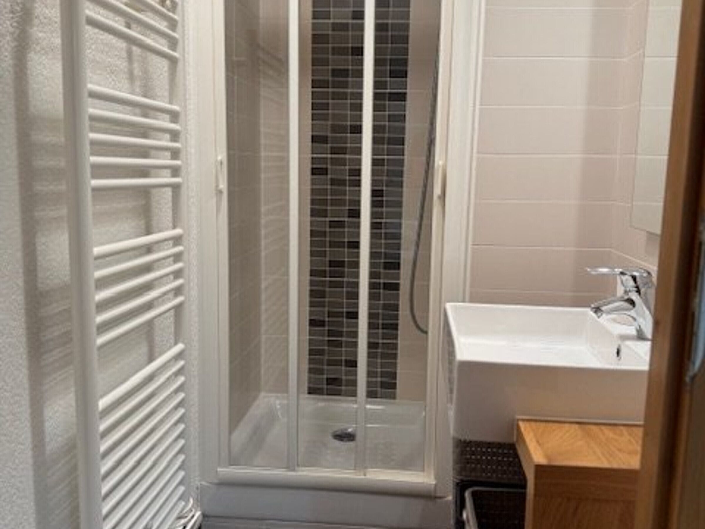 A bathroom with a shower, a sink, and a small wooden cabinet.