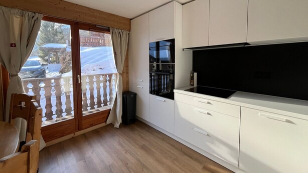 A modern kitchen with white cabinets, a black stove, and a large TV. - Cozy apartment in Châtel with balcony, 3 bedrooms, wifi, garage (Châtel)