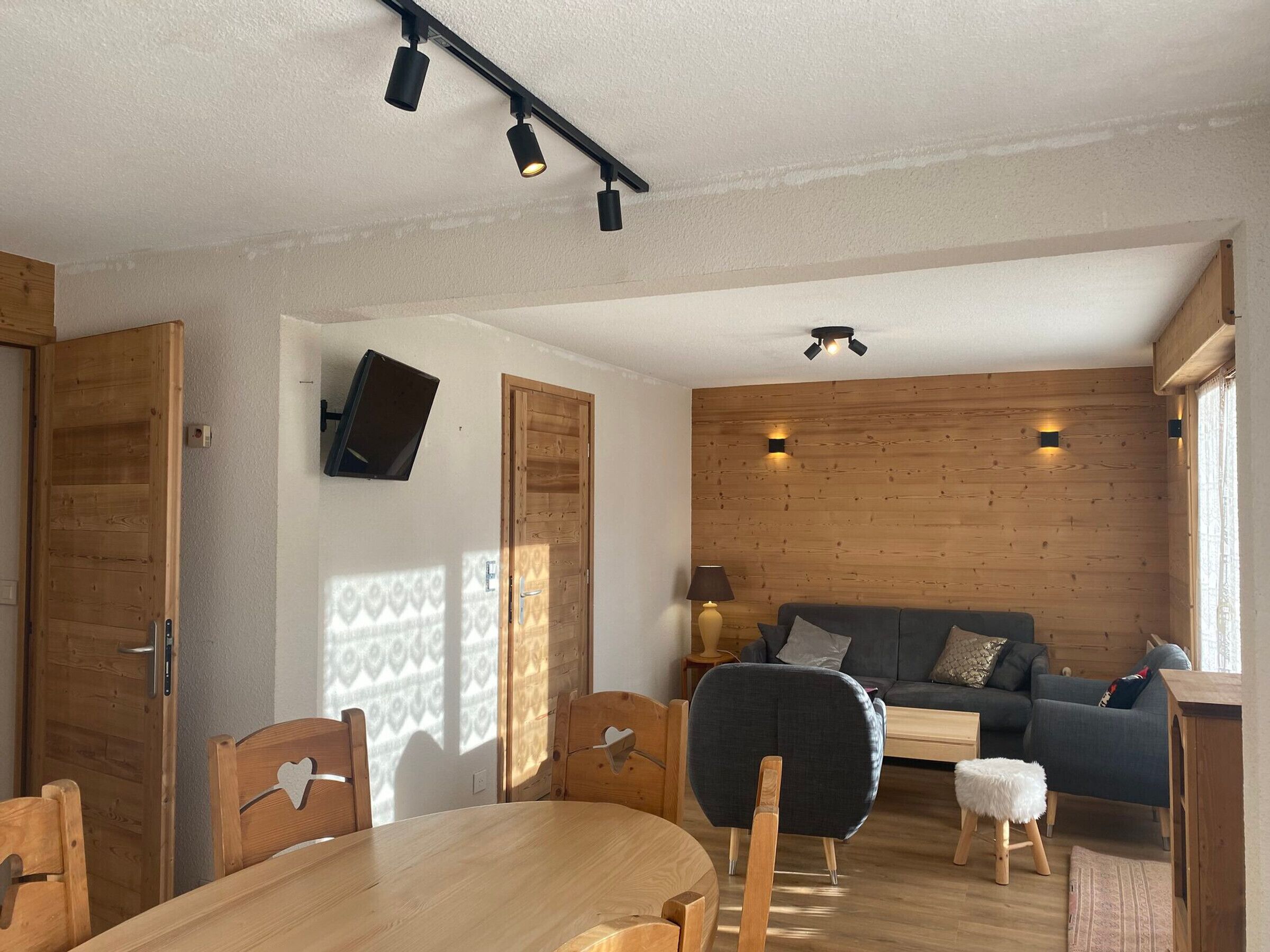 A cozy living room with a wooden wall, a sofa, a coffee table, and a TV mounted on the wall.