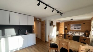 A modern kitchen with white cabinets, a wooden dining table, and a wooden ceiling with track lighting. - Cozy apartment in Châtel with balcony, 3 bedrooms, wifi, garage (Châtel)