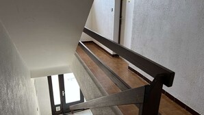 Eine Treppe mit hölzernem Geländer und Blick auf einen mit Fliesen belegten Boden, der zu einer Tür führt.