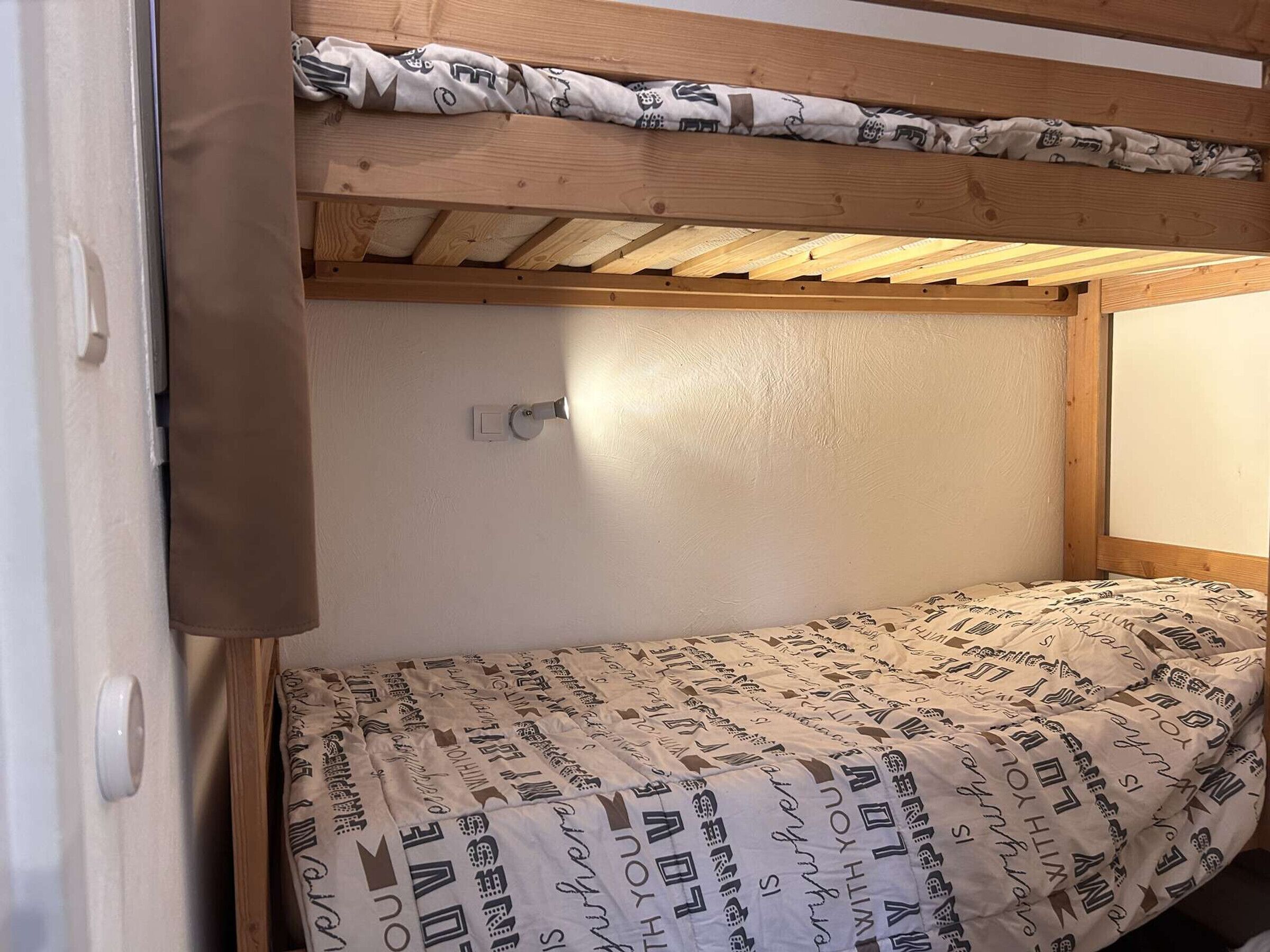 Un letto a castello con materasso decorato, una testiera in legno e un piccolo faretto a parete.