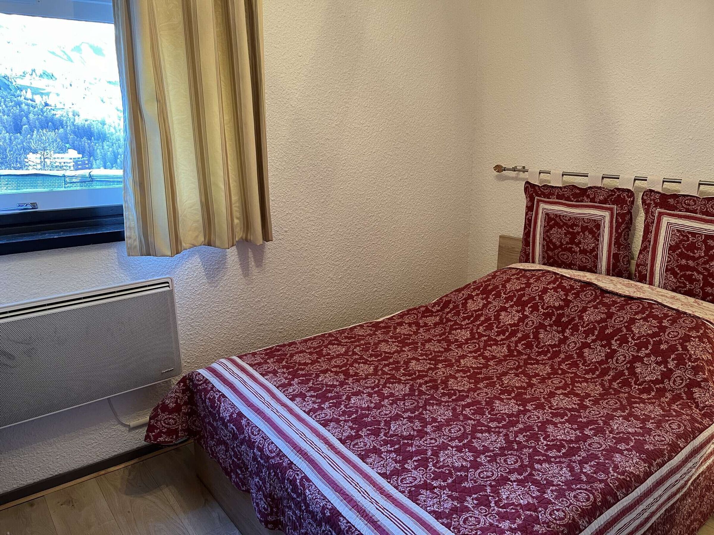 Ett sovrum med en stor säng, ett fönster med gardiner och ett element.