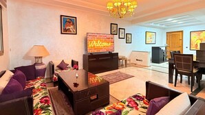 Ein Wohnzimmer mit einer Couch, einem Fernseher, einer Chandelüster und einem Essbereich mit Stühlen und einem Tisch.