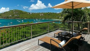 A wooden deck with lounge chairs and an umbrella, overlooking a turquoise sea with boats and a green hill in the background. - Enjoy the life at Villa Adagio, St John, Chocolate Hole in t (Cruz Bay)
