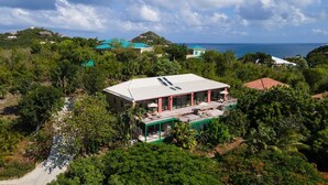 A large house with a flat roof, surrounded by dense greenery and a clear view of the ocean. - Enjoy the life at Villa Adagio, St John, Chocolate Hole in t (Cruz Bay)