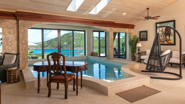 A pool area with a table and chairs, a chair with a cushion, and a view of the outside. - Enjoy the life at Villa Adagio, St John, Chocolate Hole in t (Cruz Bay)